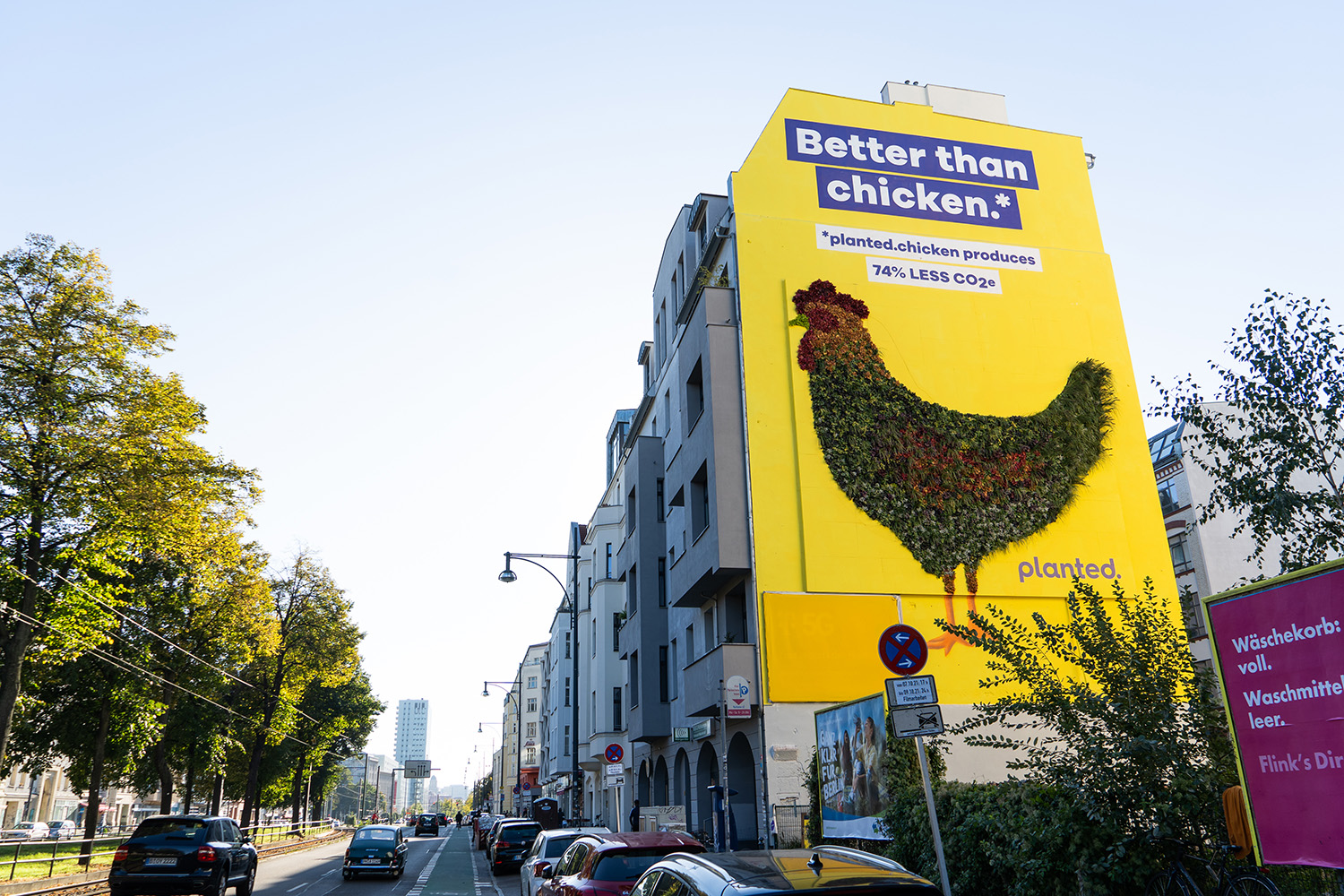 The finished yellow ‘Better than chicken.*’ mural with a chicken made of plants, seen from the street